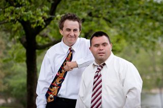 A portrait photo of two young gentlemen wearing white shirt and ties in front of green trees.