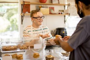A young man with down syndrome serving a customer at a bakery.