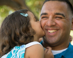 Father holding his young daughter, she kisses his cheek