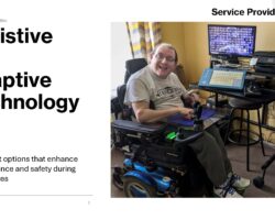 Assistive and Adaptive Technology “A smiling man in a blue power wheelchair uses a mounted adaptive communication device and computer monitor in a room.”